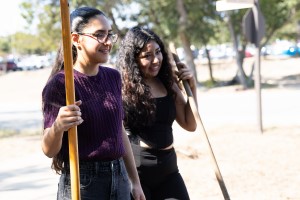 Two CTX students holding gardening tools smile as they serve in the environmental stewardship planting party